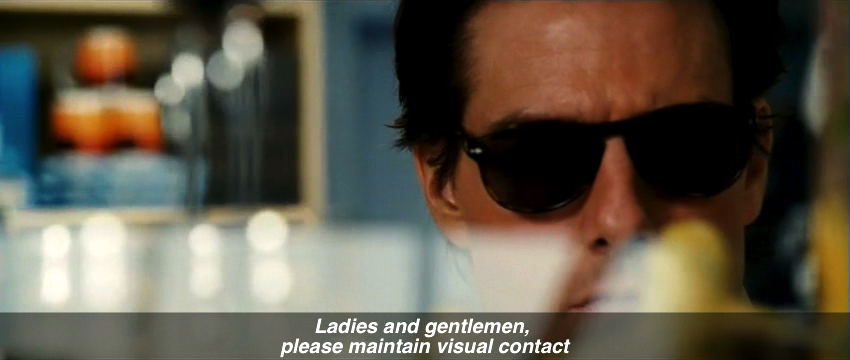 A close-up frame from Knight and Day showing Roy Miller (Tom Cruise) wearing sunglasses, captioned with an airport PA announcement.