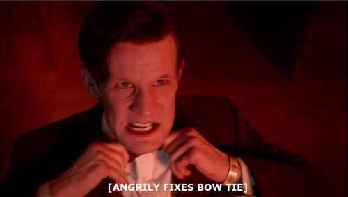 An image of the Eleventh Doctor (Matt Smith) from Doctor Who grimacing as both of his hands pull on his bow tie. Caption: [ANGRILY FIXES BOW TIE]